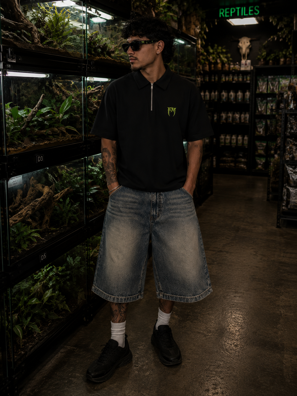 Person wearing sunglasses and a black shirt with a logo in a pet store with reptile tanks.